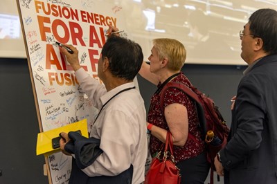''Fusion energy for all, all for fusion energy!'' Participants were invited to sign the panel that stood on the stage in the amphitheatre for the duration of the workshop. Here, Domestic Agency heads Kathy McCarthy (US ITER) and Kijung Jung (ITER Korea). (Click to view larger version...)